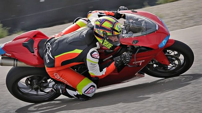 A motorcyclist leaning into a sharp turn on a red sport bike at a racetrack.