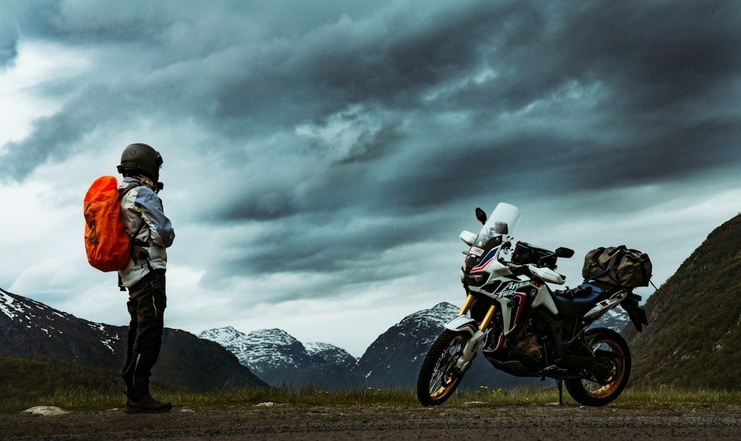 Motorcyclist and adventure bike beside snowy alpine mountains under storm clouds