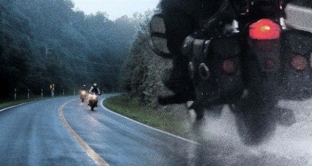 Motorcyclists ride along a wet, curving road in heavy rain